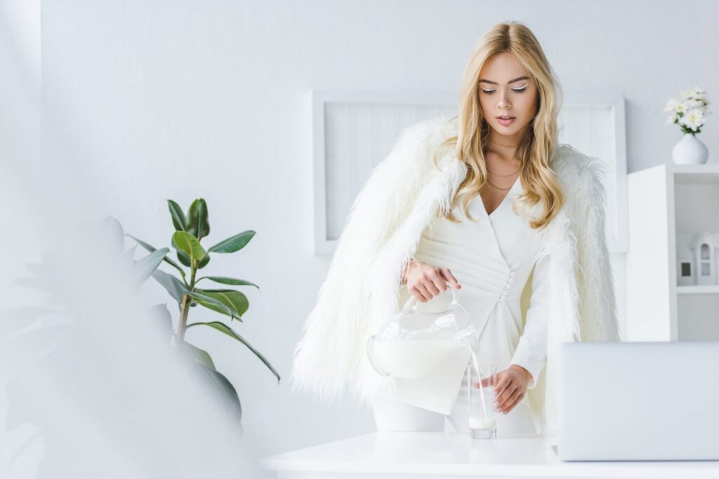 fashionable attractive woman in fur coat pouring milk into glass 